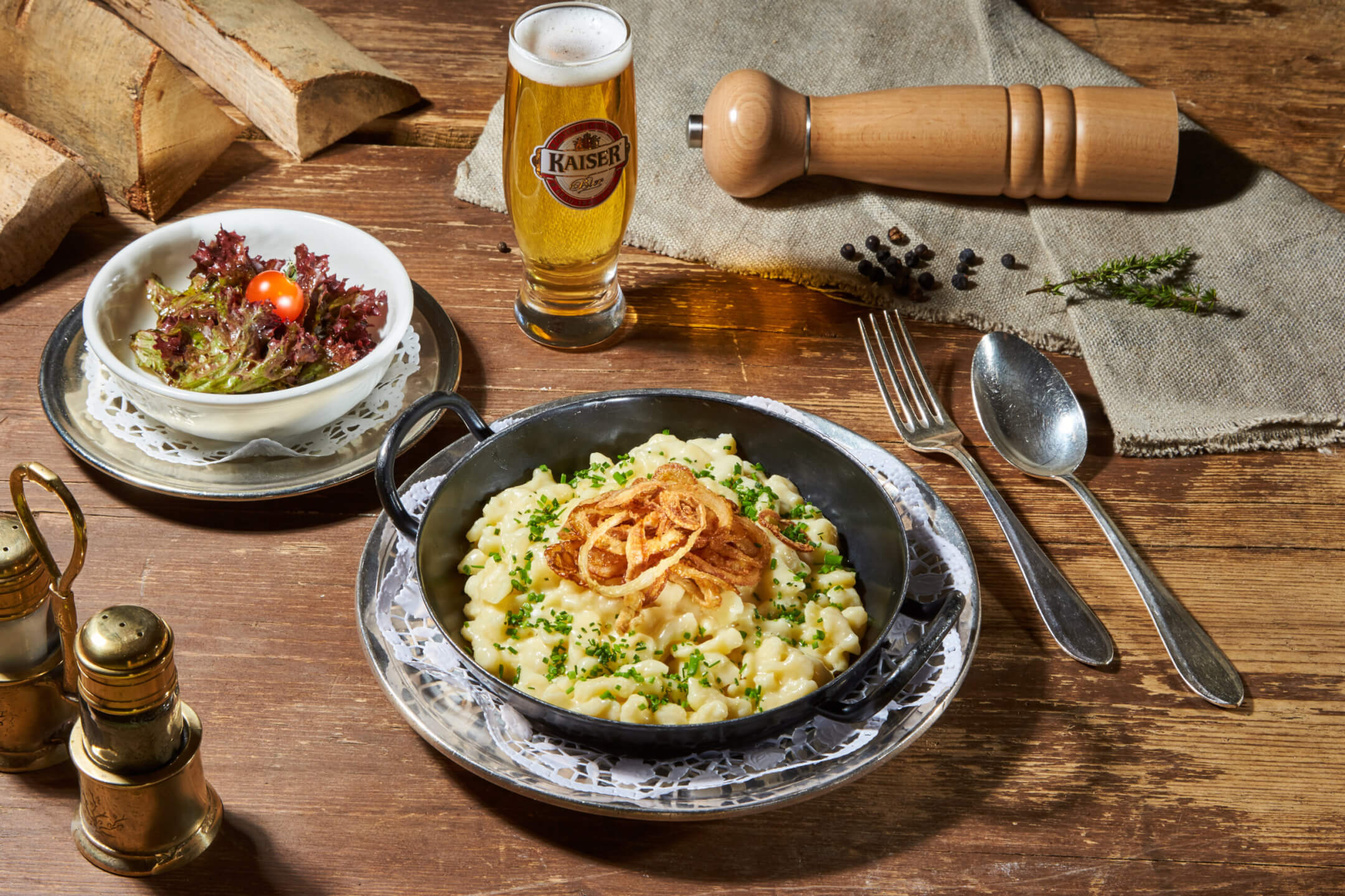 Käsespätzle serviert in der Eisenpfanne mit Salat und einem Glas Bier